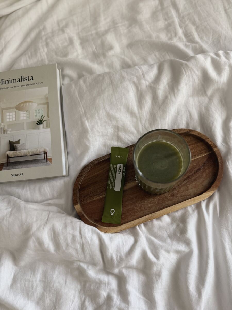 A greens drink and a book on a wooden tray in bed